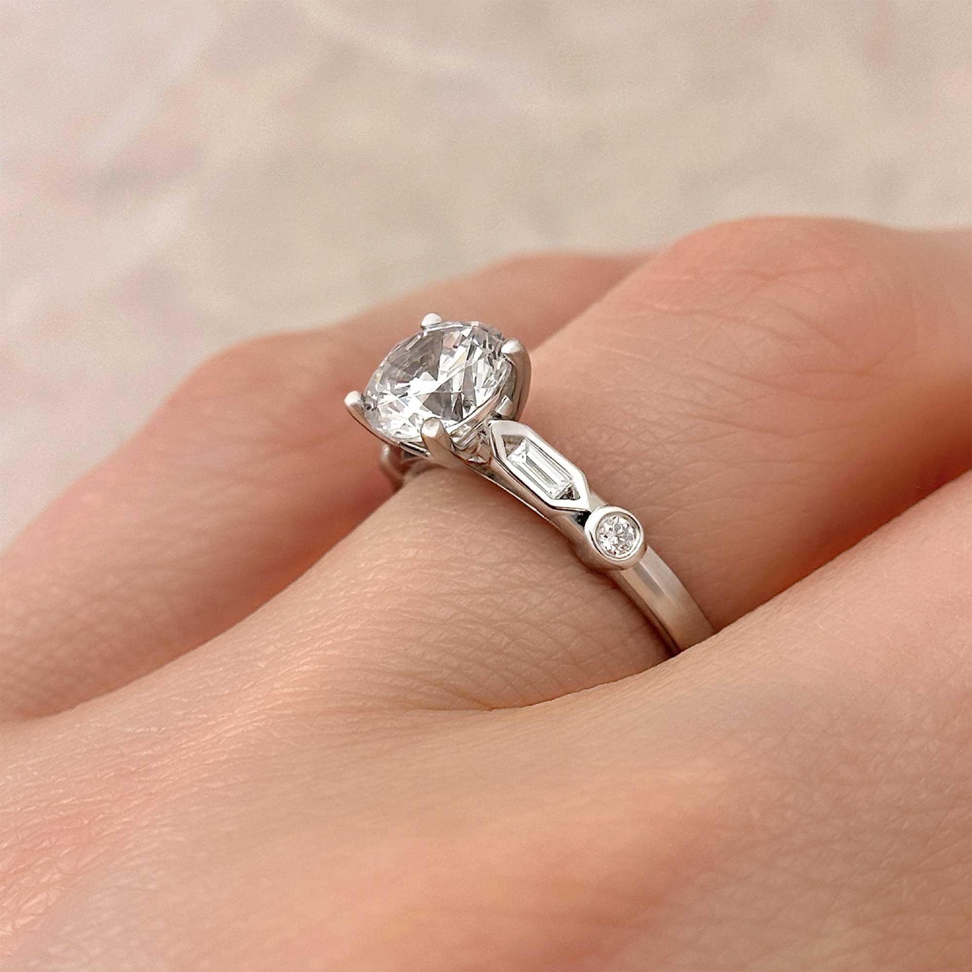 art deco revival round brilliant diamond engagement ring with diamond accents on finger