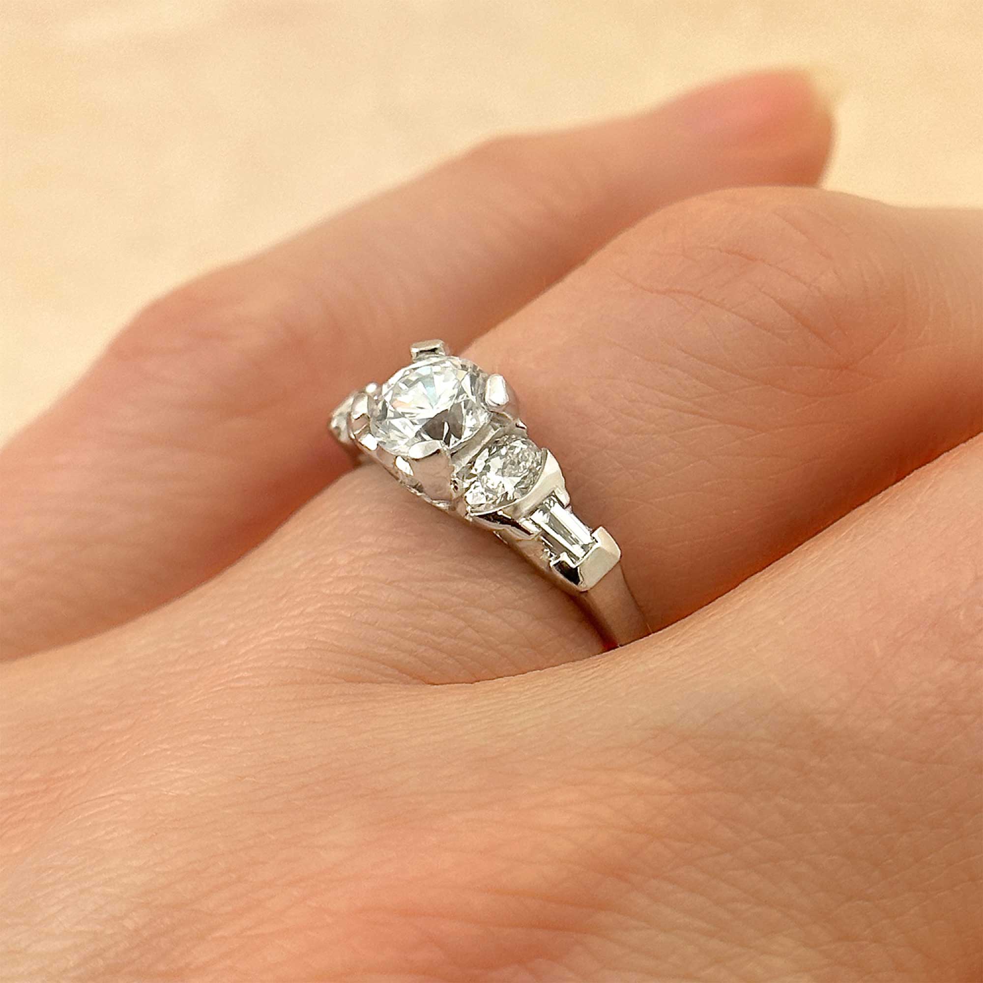 round brilliant diamond art deco style ring with oval and baguette diamond accents on finger